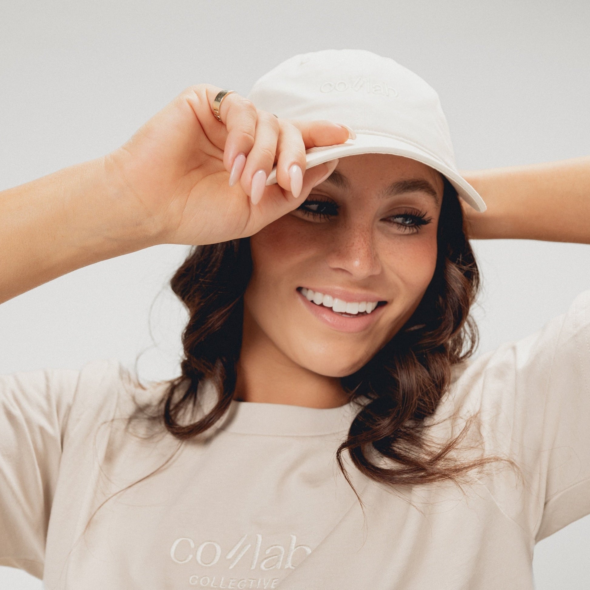 Woman wearing a white cap and beige t-shirt with 'co//lab' branding on a light background