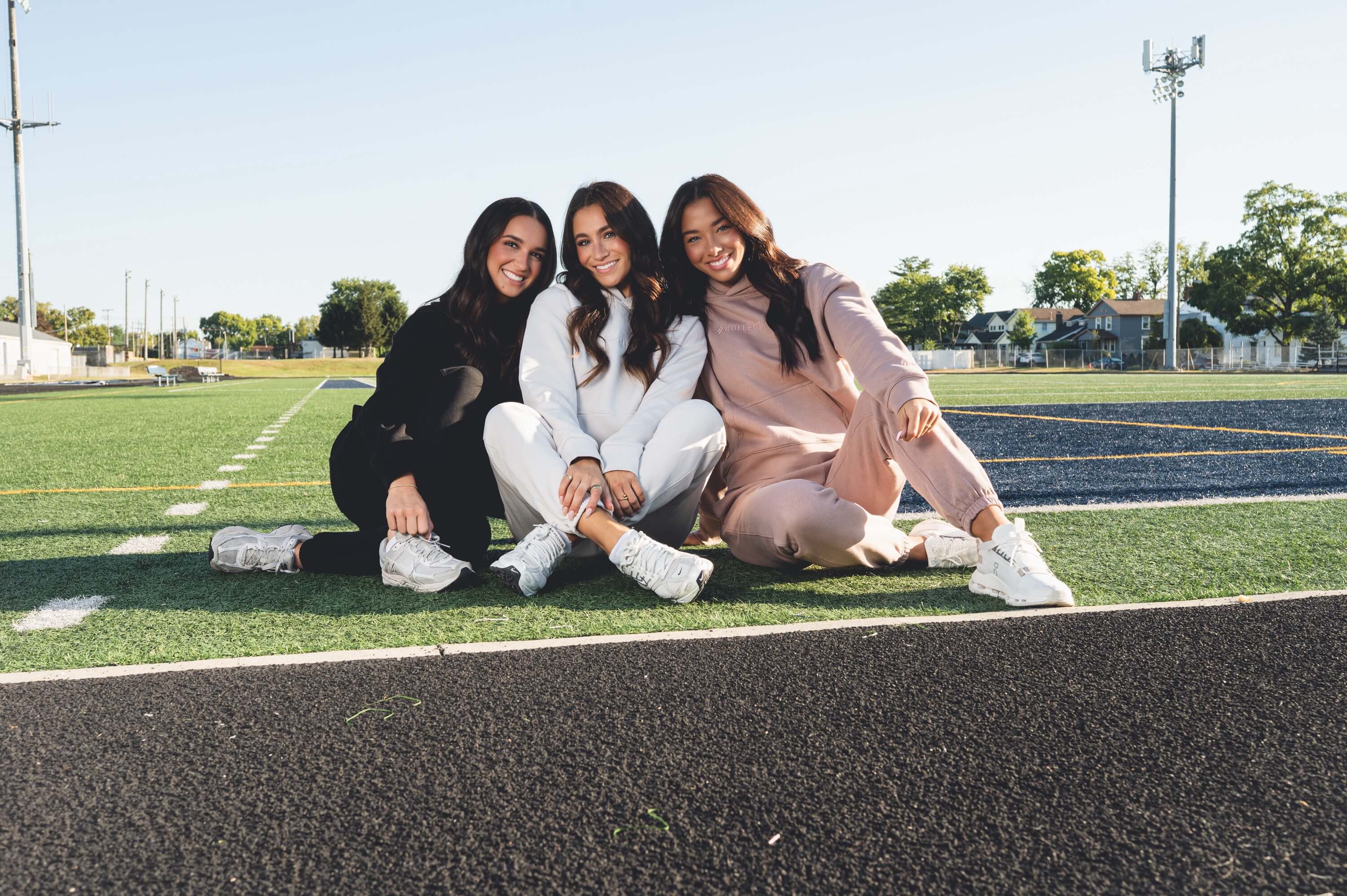 Three young women sitting on a track and field, posing for a photo.